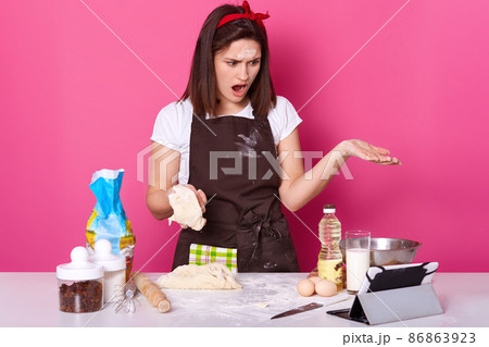 Close up view of baker kneading dough for homemade bread, has astonised facial expression, stands with open mouth, uses ipod for serching better recipe in Internet. Copy space for your advertisment. Close up view of baker kneading dough for homemade bread, has astonised facial expression, stands with open mouth, uses ipod for serching better recipe in Internet. Copy space for your advertisment. 86863923