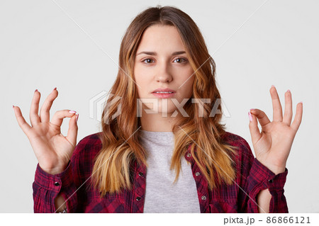 Photo of attractive young woman with dyed hair, makes okay gesture with both hands, confirms somebodys idea, gestures indoor, isolated over white background. People and body language concept Photo of attractive young woman with dyed hair, makes okay gesture with both hands, confirms somebodys idea, gestures indoor, isolated over white background. People and body language concept 86866121