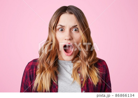 Shocked stupefied female student, opens mouth widely, being surprised to know that tomorrow is final exam, wears checkered shirt, isolated over pink background. Negative human emotions concept Shocked stupefied female student, opens mouth widely, being surprised to know that tomorrow is final exam, wears checkered shirt, isolated over pink background. Negative human emotions concept 86866134
