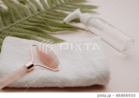 Roller on a towel and beauty product with a fern leaf on a pink background 86866930
