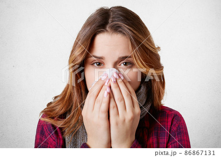 Close up portrait of beautiful woman sneezes and coughs, uses tissue, rubs nose, has bad cold, isolated over white background. Low spirited desperate woman suffers from cold and running nose 86867131