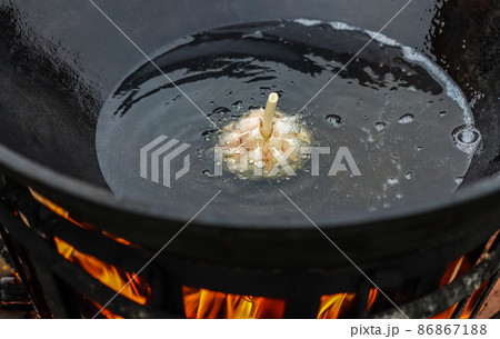 Cooking rice pilaf in a large cast iron pot over a fire. Garlic bulb in boiling oil Cooking rice pilaf in a large cast iron pot over a fire. Garlic bulb in boiling oil 86867188