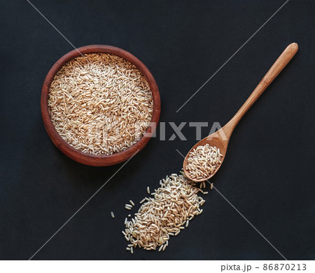 Brown rice in a wooden bowl with wooden spoon on black background, top view Brown rice in a wooden bowl with wooden spoon on black background, top view 86870213