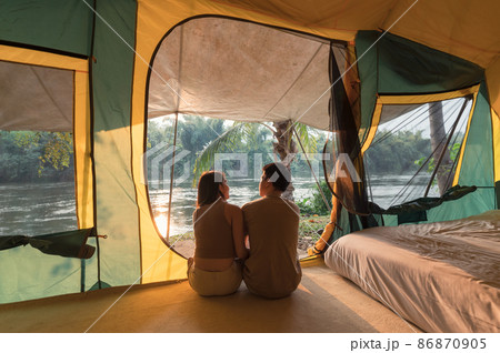 Young asian couple relaxing inside a tent on campsite in natural park Young asian couple relaxing inside a tent on campsite in natural park 86870905