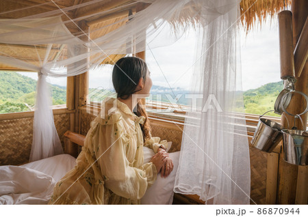 Asian woman resting on the bed and looking the mountain by window Asian woman resting on the bed and looking the mountain by window 86870944