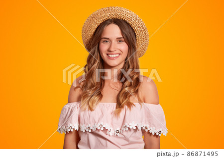 Waist up portrait of delighted beautiful young female traveller with broad smile, healthy pure skin, dressed in summer hat and blouse, poses in studio, rejoices summer vacations. Recreation concept Waist up portrait of delighted beautiful young female traveller with broad smile, healthy pure skin, dressed in summer hat and blouse, poses in studio, rejoices summer vacations. Recreation concept 86871495