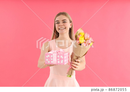 Young woman with bouquet and gift box on pink background Young woman with bouquet and gift box on pink background 86872055