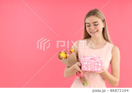 Young woman with bouquet and gift box on pink background Young woman with bouquet and gift box on pink background 86872104