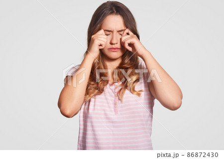 Photo of displeased young girl rubs eyes, being in low spirit, wears casual domestic clothes, poses against white background. Woman had bad sleep at night. Bedding concept. People and tiredness Photo of displeased young girl rubs eyes, being in low spirit, wears casual domestic clothes, poses against white background. Woman had bad sleep at night. Bedding concept. People and tiredness 86872430