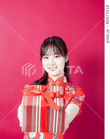 Portrait of a young asian woman wearing traditional cheongsam qipao dress holding gift isolated over red background. Portrait of a young asian woman wearing traditional cheongsam qipao dress holding gift isolated over red background. 86873016