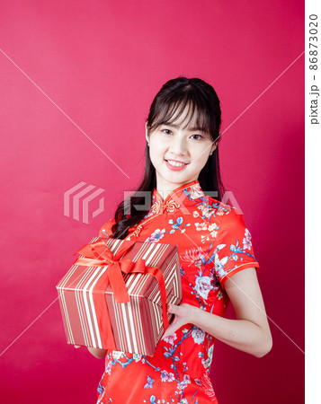 Portrait of a young asian woman wearing traditional cheongsam qipao dress holding gift isolated over red background. Portrait of a young asian woman wearing traditional cheongsam qipao dress holding gift isolated over red background. 86873020