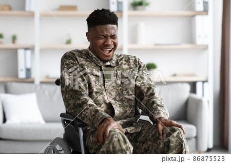 Unhappy black soldier in wheelchair tocuhing his legs and screaming Unhappy black soldier in wheelchair tocuhing his legs and screaming 86875523