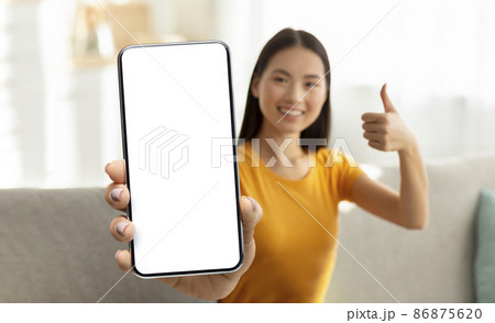 Cheerful young asian woman showing smartphone with blank screen 86875620