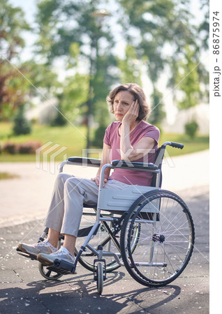 Disabled mid aged woman sitting in a wheel-chair with an unhappy look 86875974