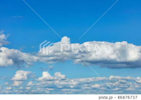 Volumetric white clouds float in even rows across a bright blue sky. 86876737