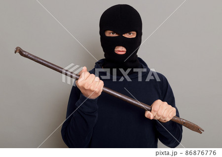An evil insidious criminal thief man with an iron crowbar in his hands, is going to break down the door, rob an apartment, looks at camera with a sly and insidious expression on his face. 86876776
