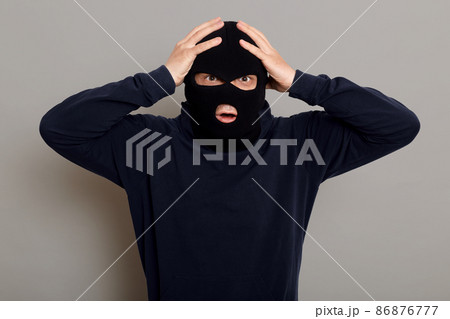 Shocked and frightened criminal, thief catching on place of committing crime, looking at camera with frightened eyes, holding his head, does not understand what to do, isolated over gray background. 86876777