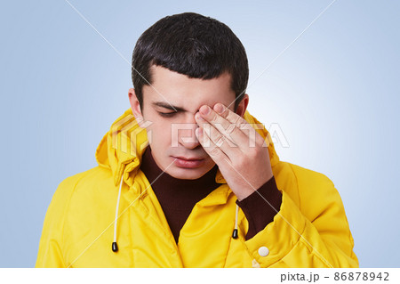 Portrait of upset unhappy tired man tries to recollect something in his mind, covers eye with hand, closes eyes, tries to concentrate, wears stylish clothes, isolated over light blue background Portrait of upset unhappy tired man tries to recollect something in his mind, covers eye with hand, closes eyes, tries to concentrate, wears stylish clothes, isolated over light blue background 86878942