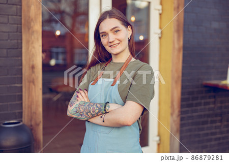 Cheerful female barista standing outside coffee shop 86879281