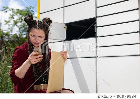 Out of curiosity, she immediately checks on her mobile phone who of her friends sent her the package. He crouches at the parcel locker. Out of curiosity, she immediately checks on her mobile phone who of her friends sent her the package. He crouches at the parcel locker. 86879934