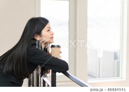手すりに肘をついてコーヒーカップを持ってリラックスするビジネスウーマン 手すりに肘をついてコーヒーカップを持ってリラックスするビジネスウーマン 86884541
