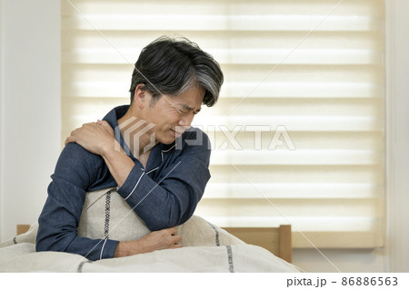 ベッドに座って肩を手で押える中高年男性 86886563