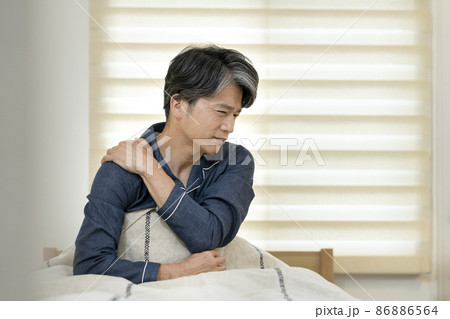 ベッドに座って肩を手で押える50代の男性 86886564