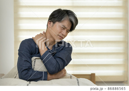 ベッドに座って首を手で押える中高年男性 86886565