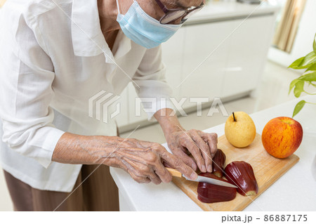Asian old elderly people in a medical face mask,cutting the rose apple into slices,senior woman eating fresh fruit or nutritious food while stay at home,nutritional,healthy food,health care concept Asian old elderly people in a medical face mask,cutting the rose apple into slices,senior woman eating fresh fruit or nutritious food while stay at home,nutritional,healthy food,health care concept 86887175