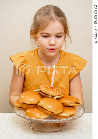 a little girl makes a wish and blows out a candle on a hamburger cake. 86888582