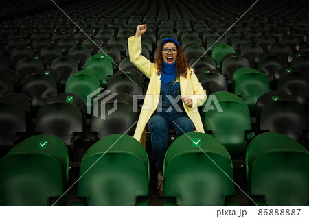 Caucasian woman cheers for a sports team at the stadium. The girl watches the match at the stadium alone. Caucasian woman cheers for a sports team at the stadium. The girl watches the match at the stadium alone. 86888887