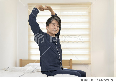ベッドに座ってストレッチをするパジャマ姿の笑顔の50代の男性 ベッドに座ってストレッチをするパジャマ姿の笑顔の50代の男性 86890419