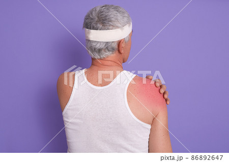 Back view of white haired senior man posing in studio against lilac wall, male being injured in gym, doing physical exercises, poses backwards, needed treatment, asks to call doctor. Health concept. 86892647