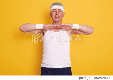 Indoor shot of senior sporty man wearing sleeveless t shirt and headband, keeping hands in front of chest, doing physical exercises, warming up, healthy lifestyle. 86892657