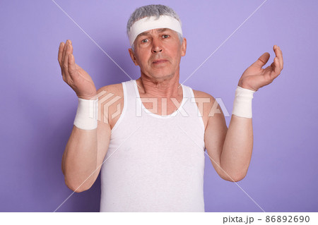 indoor shot of elderly man shrugging shoulders and spreading hands, showing helpless gesture, posing isolated over lilac studio background, senior male looks at camera with puzzled facial expression. indoor shot of elderly man shrugging shoulders and spreading hands, showing helpless gesture, posing isolated over lilac studio background, senior male looks at camera with puzzled facial expression. 86892690