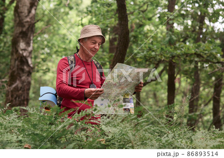 Close up portrait of traveler senior man searching right direction on map, traveling along nature. Old Tourist with map standing in amazing forest, freedom, active lifstyle, happy and health 86893514