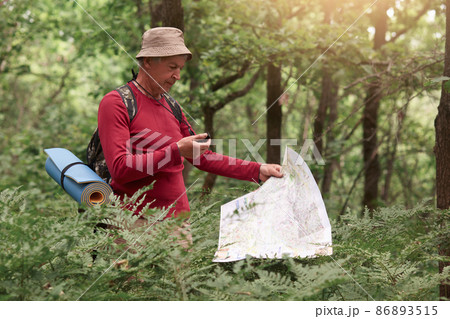 Coordination and navigation in the forest. Image of man holding compass and paper map in his hands, finding right way in wood, being lost while walking on path and enjoying beautiful nature. 86893515