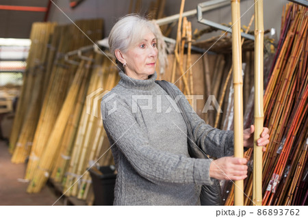 Mature woman choosing bamboo pole in store Mature woman choosing bamboo pole in store 86893762