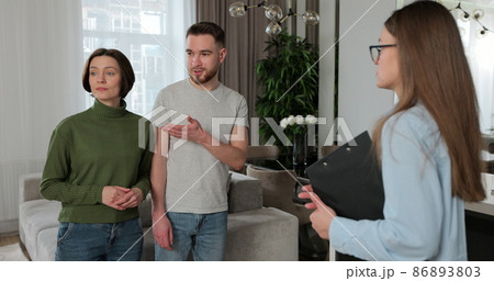 Close up of real estate agent woman shows modern house to a young couple. Young couple client rent investment. Close up of real estate agent woman shows modern house to a young couple. Young couple client rent investment. 86893803