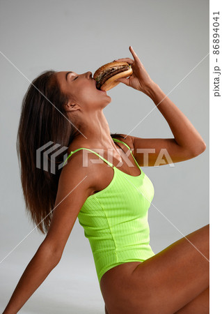 cheat meal concept. athlete woman is posing with fast food on light gray background, studio shot. young sporty woman is holding fast food close up. 86894041