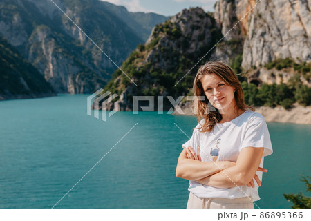 Girl tourist stands on the shore of a lake in the mountains. beautiful landscape, Piva Lake in Montenegro.. Woman is standing on the coast of Piva lake at sunset in summer. Landscape with girl, famous 86895366