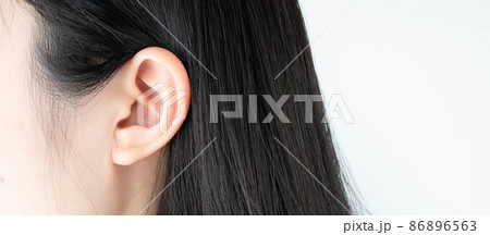 Close up of female ear in black hair over white background. Copy space. 86896563