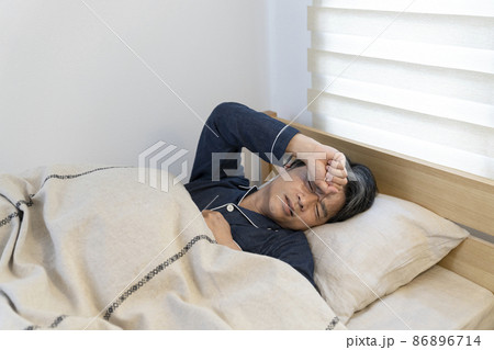 辛そうな表情で眠る50代の男性 86896714