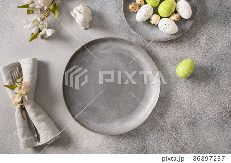 Easter festive table setting with gray plate, spring flowers and green colorful eggs. Easter festive table setting with gray plate, spring flowers and green colorful eggs. 86897237