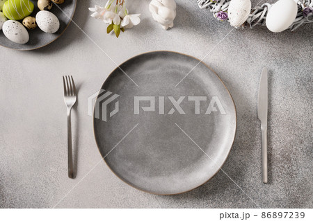Easter festive table setting with gray plate, spring flowers and green colorful eggs. Easter festive table setting with gray plate, spring flowers and green colorful eggs. 86897239