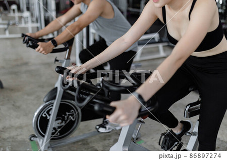 exercise concept The two sport club participants playing exercise bike machine for doing their cardio beside each other exercise concept The two sport club participants playing exercise bike machine for doing their cardio beside each other 86897274