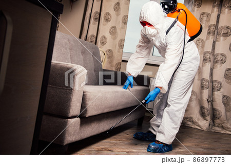 An exterminator in work clothes sprays pesticides with a spray gun. Fight against insects in apartments and houses. Disinsection of the premises 86897773