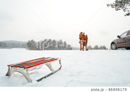 Sledge against happy family on a walk in winter forest Sledge against happy family on a walk in winter forest 86898179