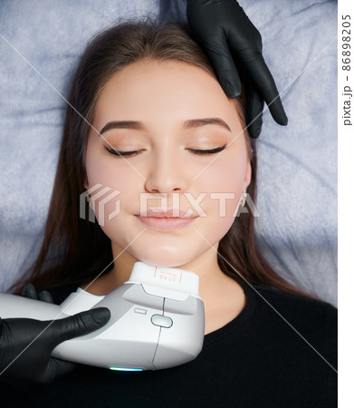 Top view portrait of young attractive woman lying and beautician doing cleaning face with special machine. Concept of process procedure for improvements skin in professional beauty salon. 86898205