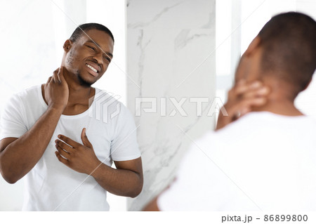 Unhappy Black Guy Suffering Neck Ache While Standing Near Mirror In Bathroom Unhappy Black Guy Suffering Neck Ache While Standing Near Mirror In Bathroom 86899800